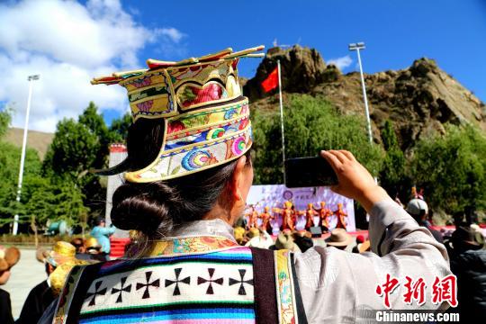 在中国文化和自然遗产日前夕，西藏山南市琼结县民族优秀服装、工艺品、舞蹈、音乐和酒文化等非遗项目集体亮相，为当地民众呈现文化饕餮盛宴。图为身着琼结达娃卓玛服饰的观众正在用手机记录非遗展演。　伦珠泽仁摄